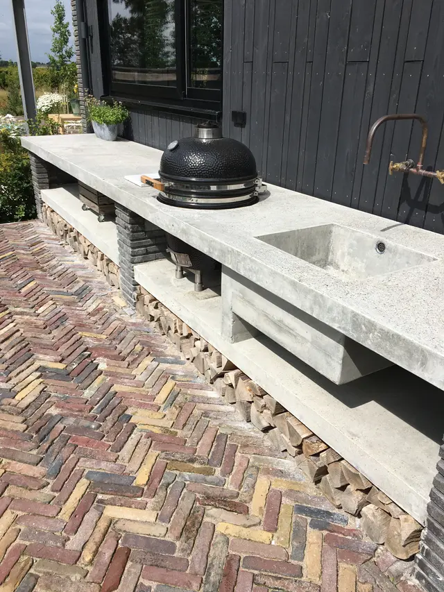 Betonnen buitenkeuken met kamado bbq langs zwarte gevel