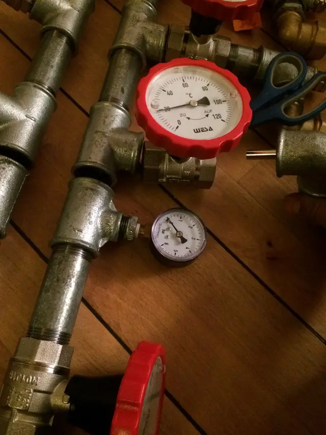 Thermometer en drukmeter tussen leidingwerk op houten vloer