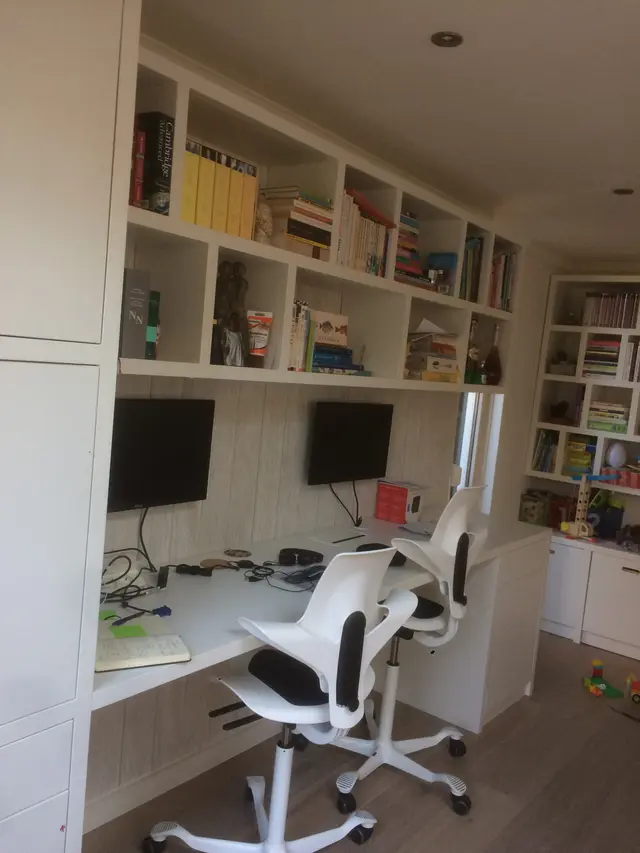 Wandkast met boeken boven bureau met twee werkplekken