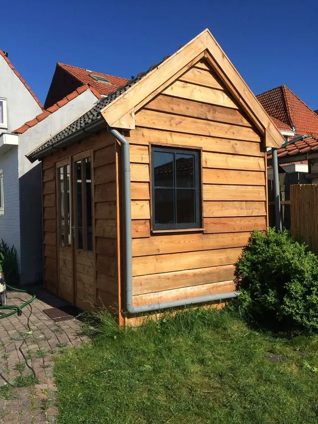 Zijaanzicht houten tuinhuisje met puntdak en raam