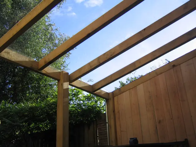 Pergola met glazen dakplaten tegen houten gevel