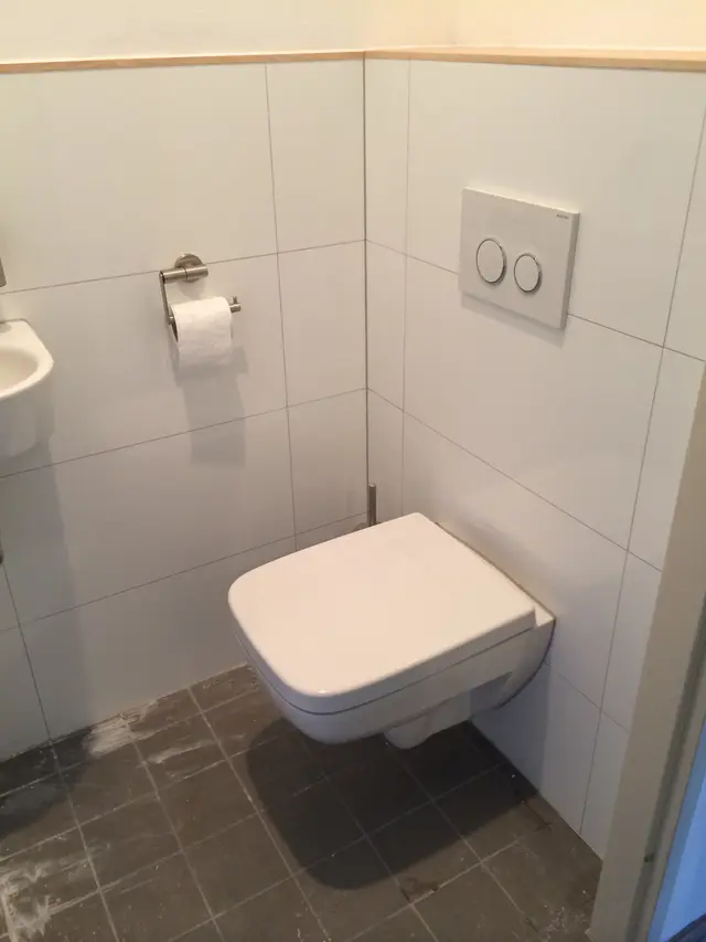 Wandcloset met bedieningsplaat in betegelde badkamer